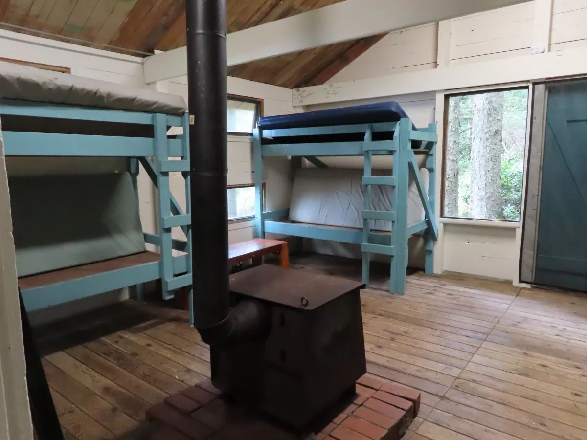 Two bunk beds against back wall. Wood stove for heating in front.