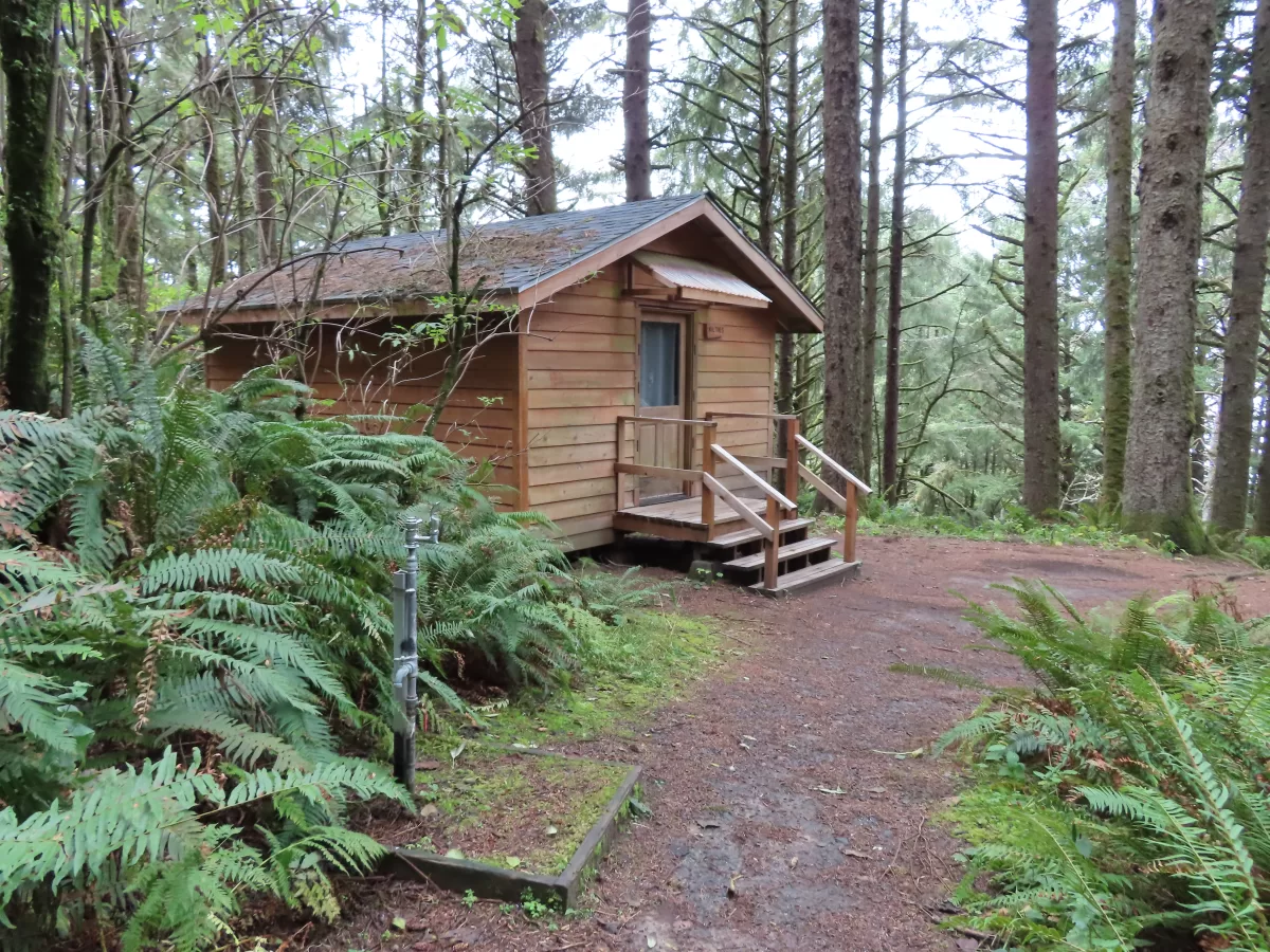 Wooden cabin with wooden stairs. Water fountain in foreground