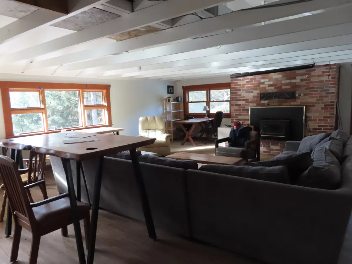 Office area with eight section couch, standing table, arm chairs and two desks. Brick fireplace behind.