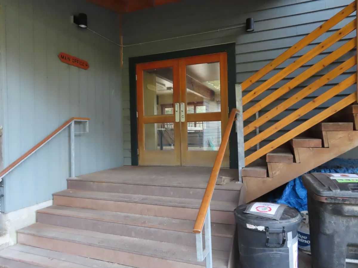 Wooden steps with railing leading up to double doors into lodge.