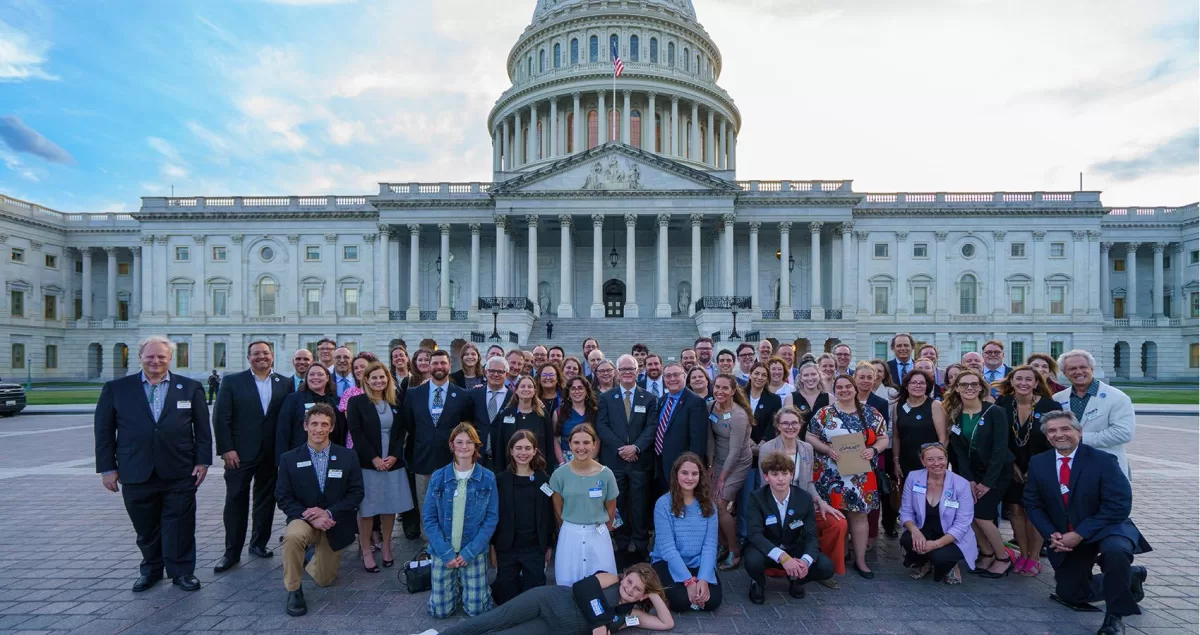 large group of adults pose in front of the US Capital Building.