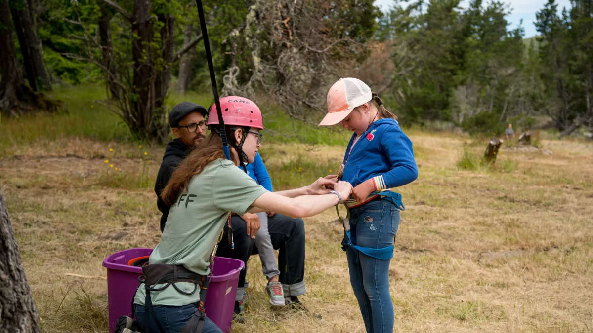 staff member helps girl adjust tree climbing harness.