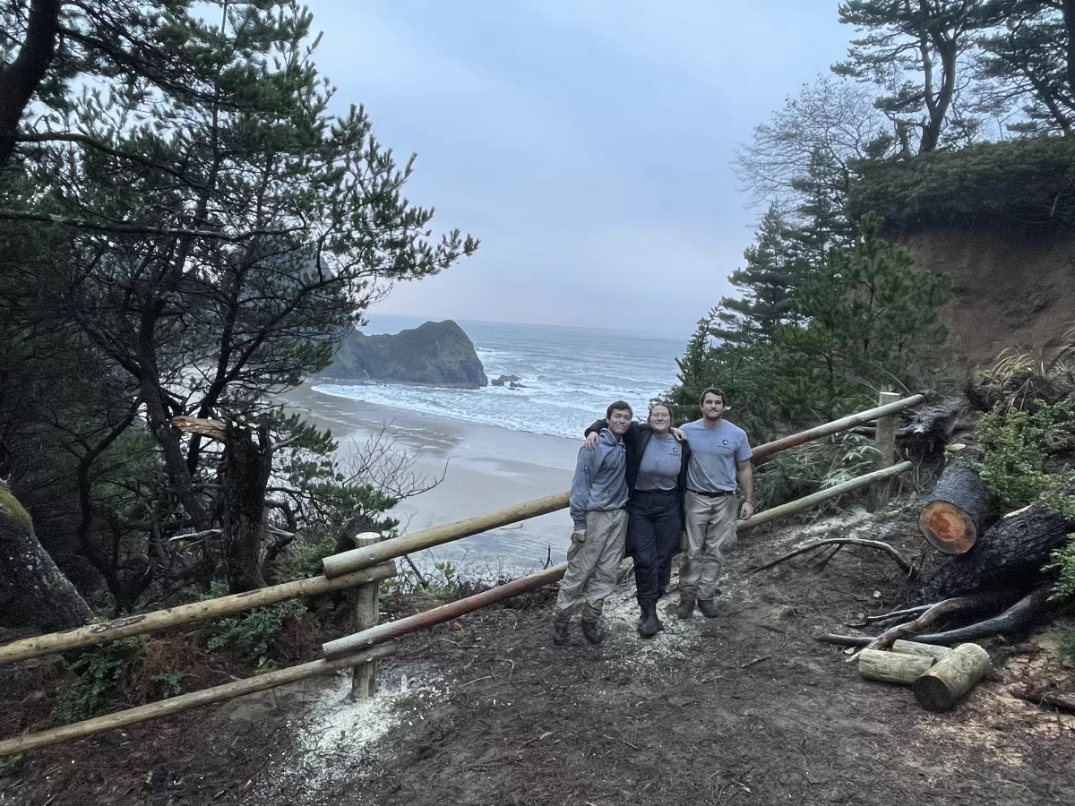 Three teens in matching shirts pose for a photo in front of the ocean. 